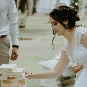 Bride playing on-site Jenga game for weddings with large wooden blocks outdoors