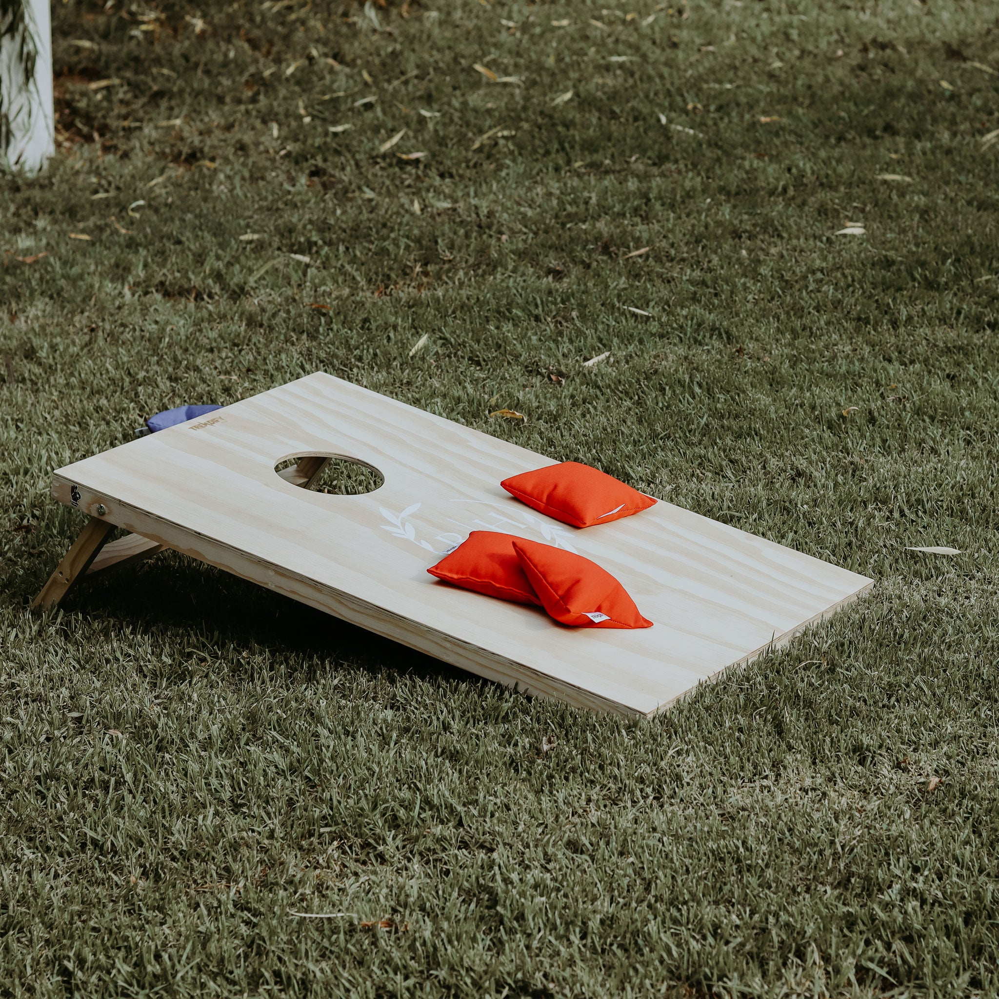 Wooden cornhole set for on-site weddings with red bean bags placed on green grass