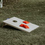 Wooden cornhole set for on-site weddings with red bean bags placed on green grass