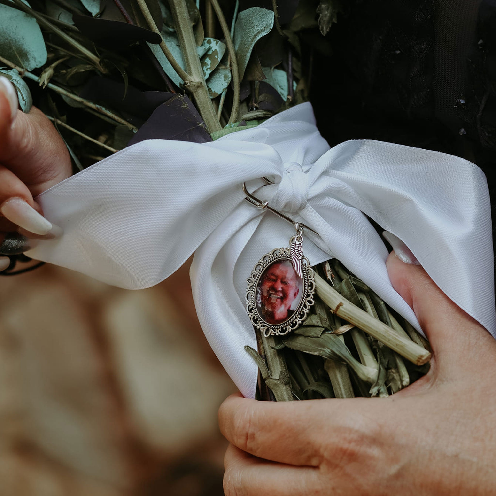 Custom wedding bouquet pendant attached to white ribbon on a bridal bouquet held by hands