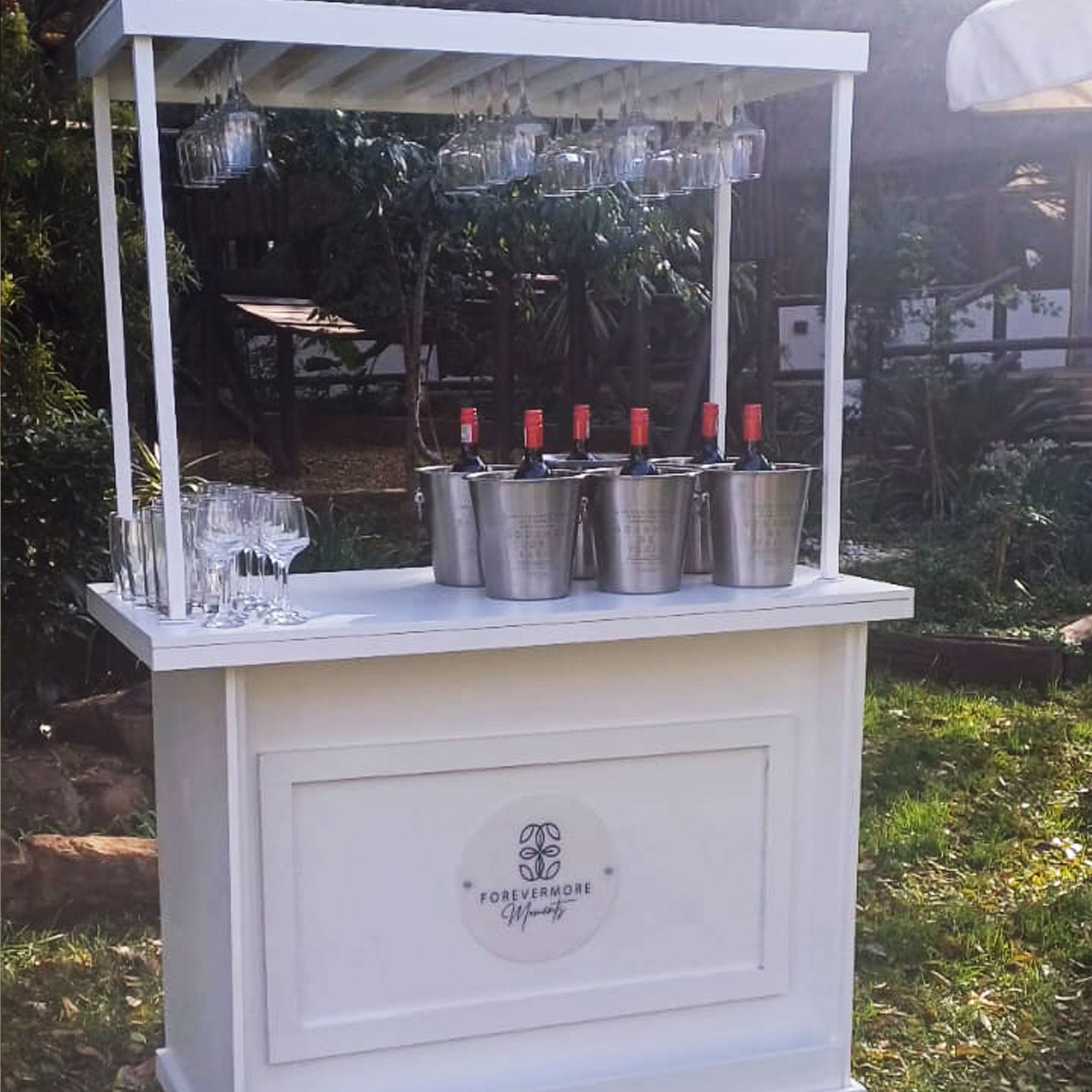 Forevermore Momentos on-site wedding reception cart with wine bottles and hanging glasses in outdoor setting