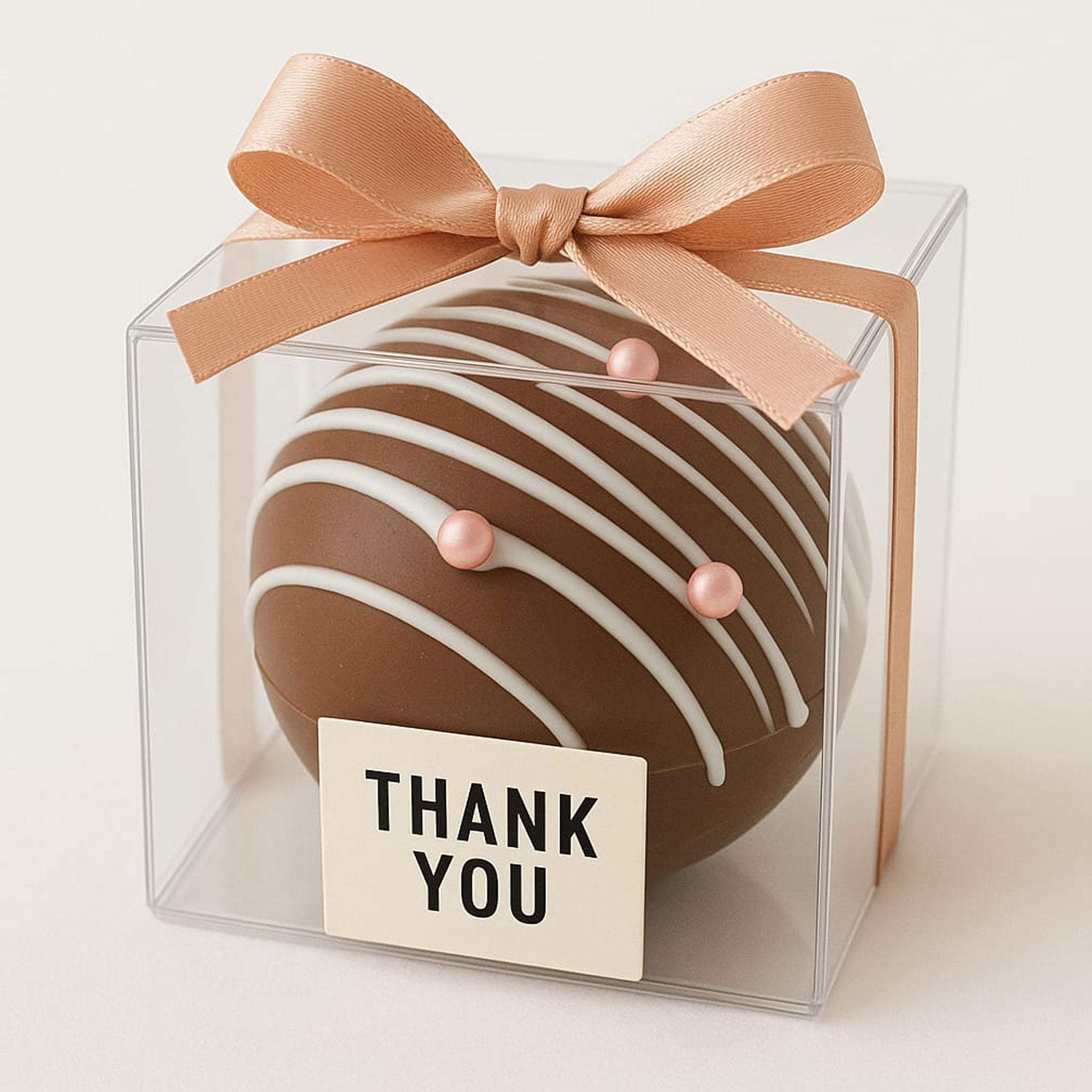 Handmade chocolate bomb gift with white drizzle and pink pearls in clear box with peach bow