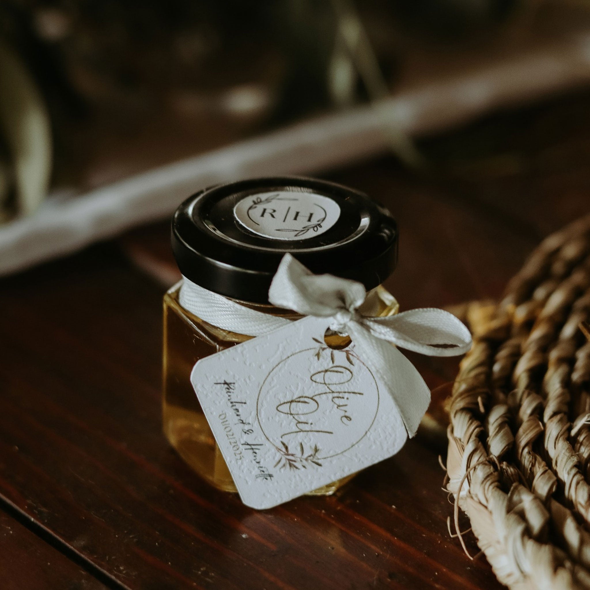 Mini olive oil or honey wedding favors with black lid and white ribbon tag on wooden surface