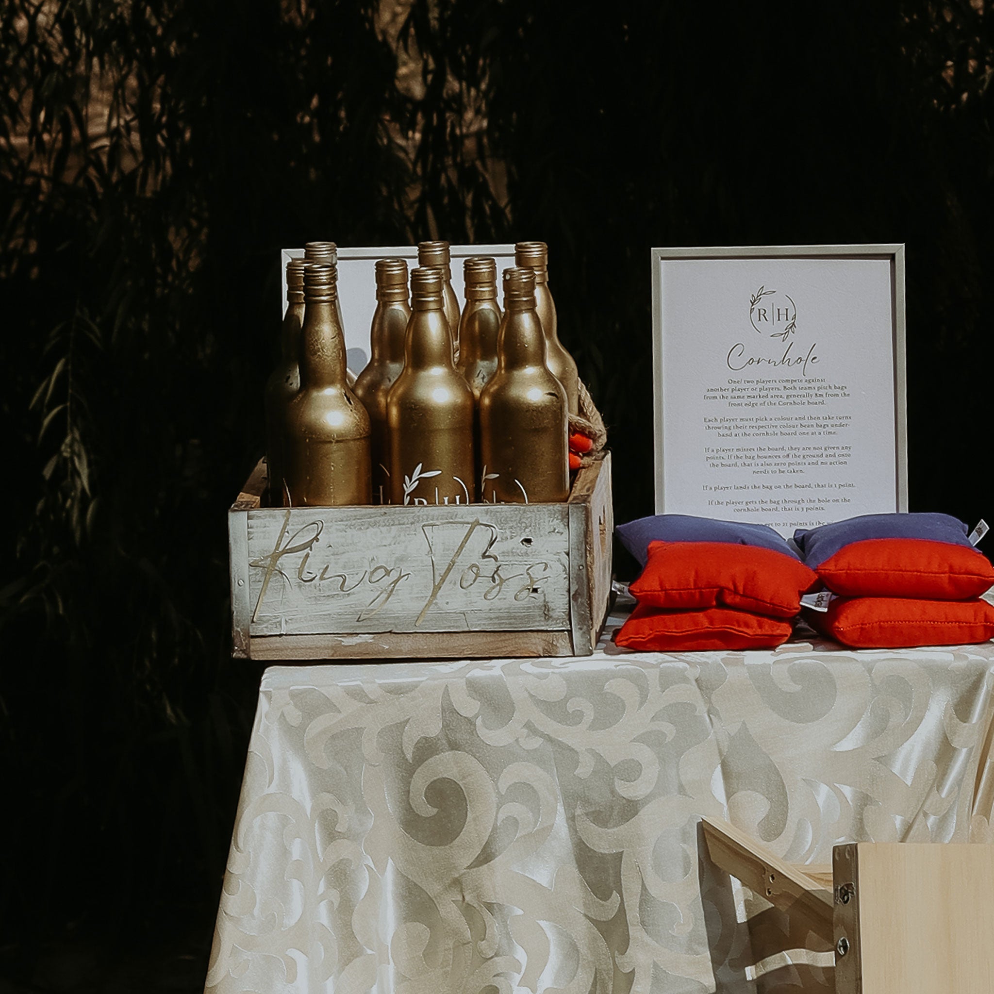 On-site wedding game ring toss rental with gold bottles and colorful bean bags on a decorated table