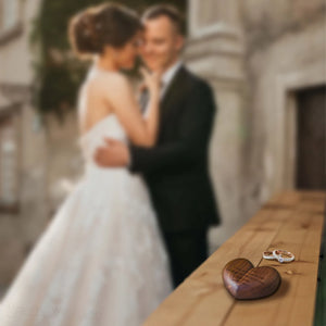 Personalized heart wood ring box placed on a wooden surface with a couple in the background