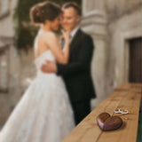 Personalized heart wood ring box placed on a wooden surface with a couple in the background