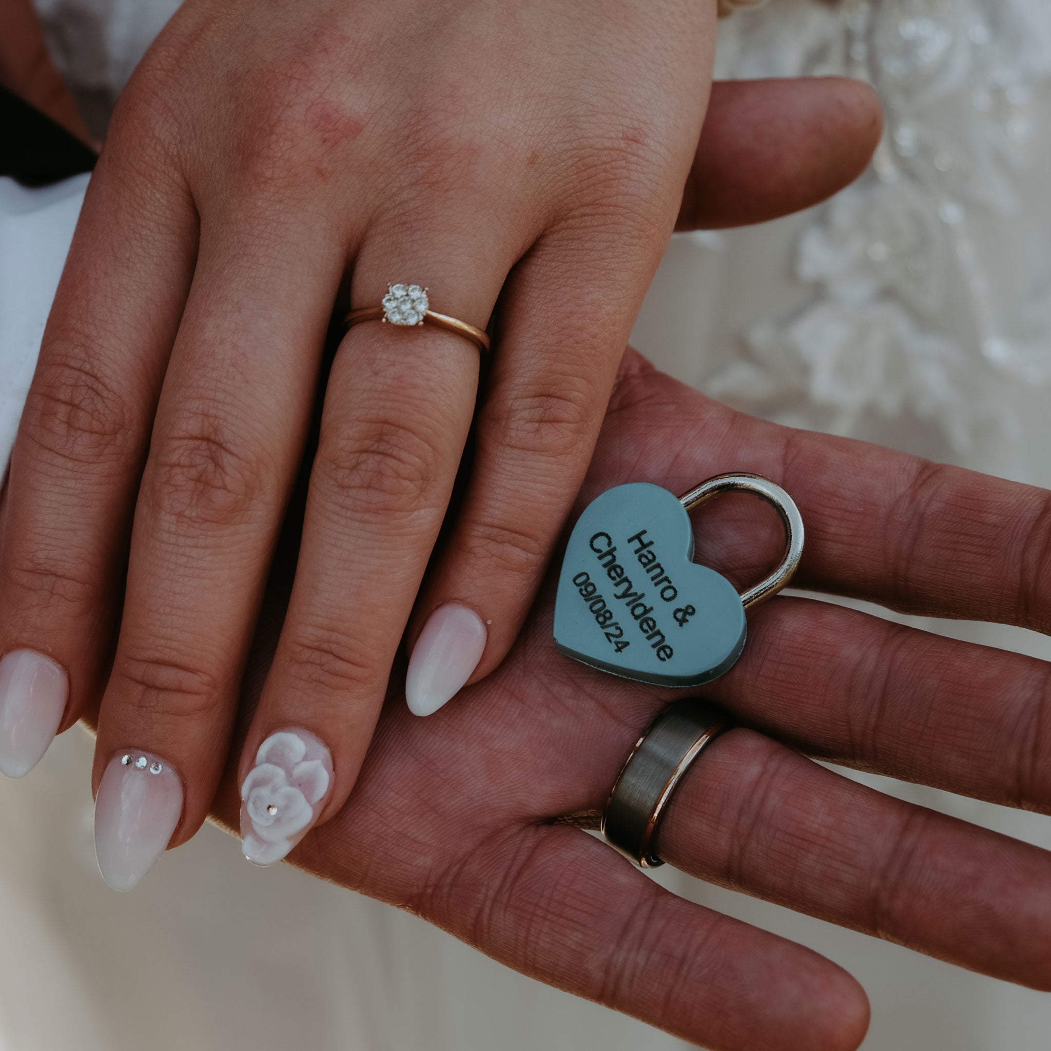 Heart-shaped personalized love locks wedding padlock engraved with names and date held by couple with wedding rings